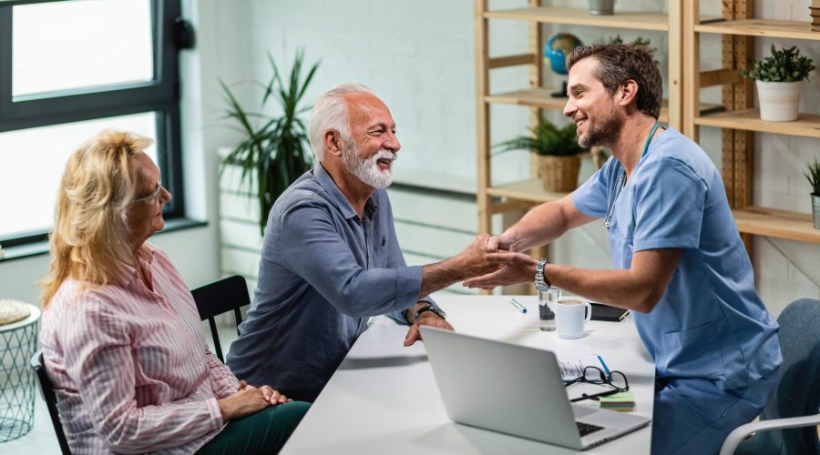 happy-male-doctor-shaking-hands-with-senior-man-who-came-medical-appointment-with-his-wife-min